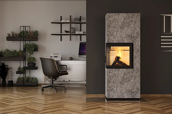 Foto einer monolith Feuerstätte der Firma CB-tec GmbH mit einer Verkleidung aus Naturstein in einem Wohnzimmer. Sichtbar ist außerdem ein Schreibtisch mit Bürostuhl und Computer.
